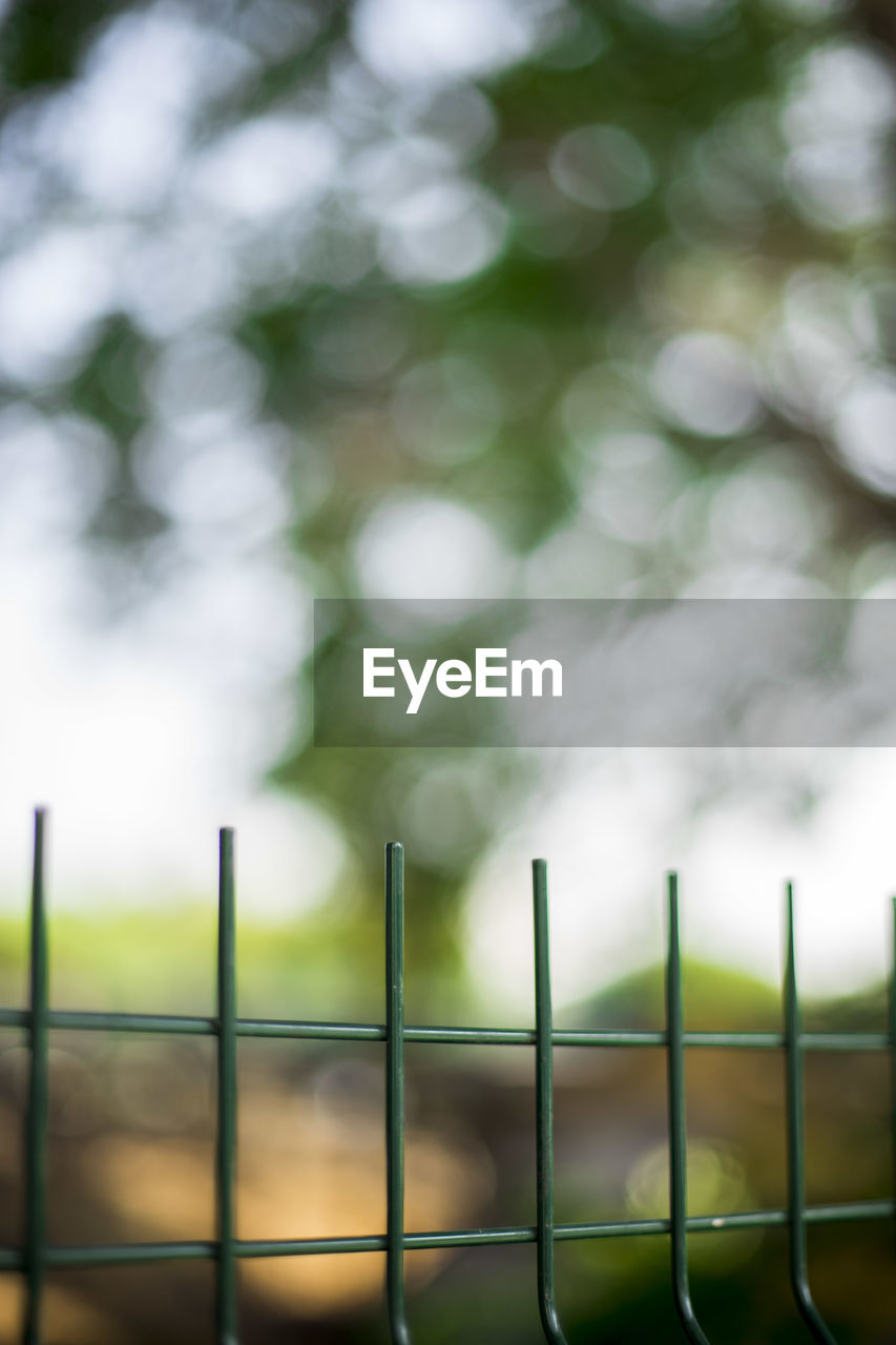 LOW ANGLE VIEW OF FENCE AGAINST BLURRED PLANTS