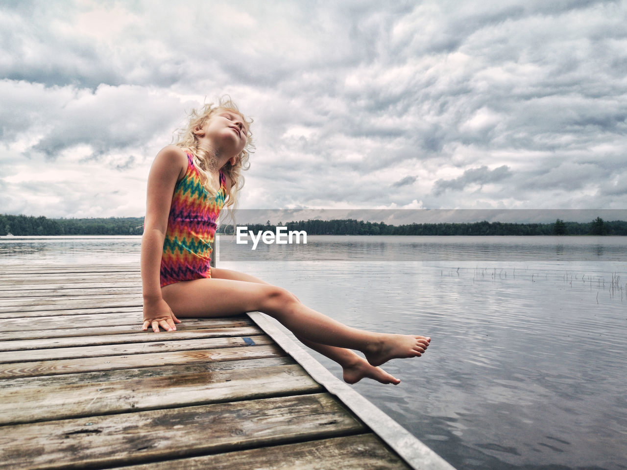 Full length of girl sitting on pier over lake against sky