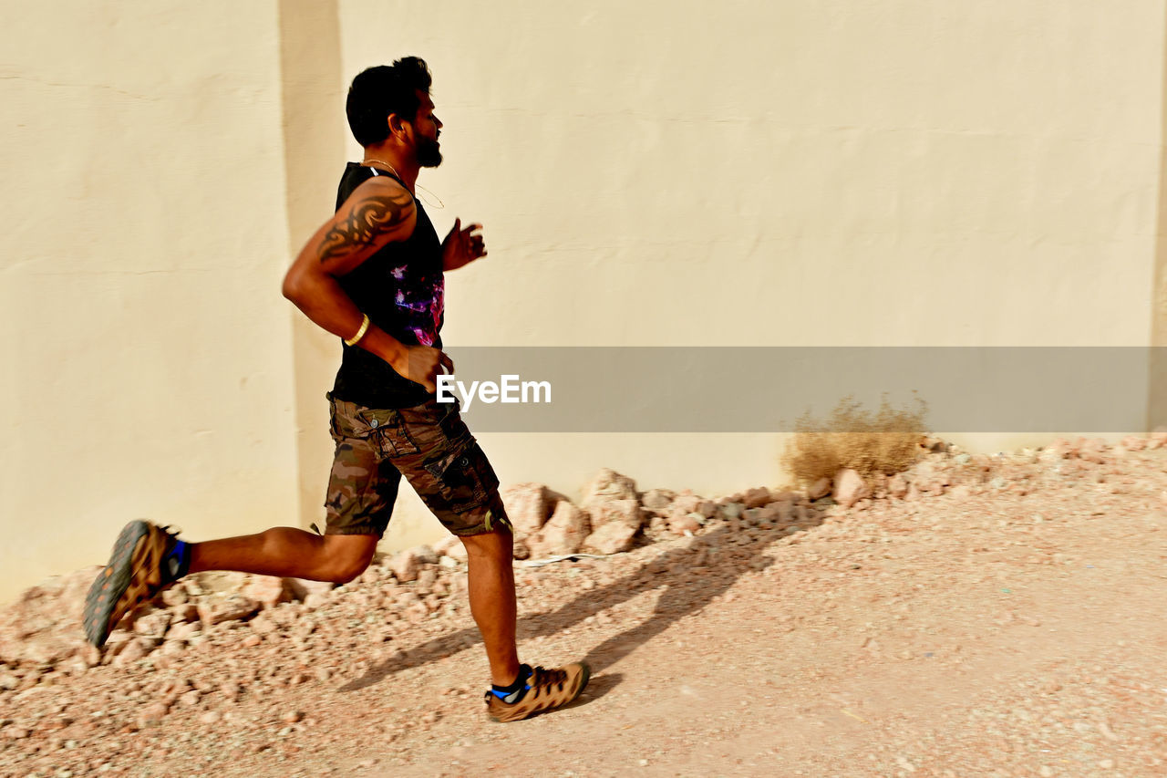 Side view of young man running by building