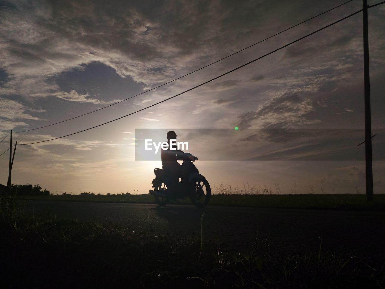 SILHOUETTE MAN RIDING BICYCLE ON FIELD AGAINST SKY