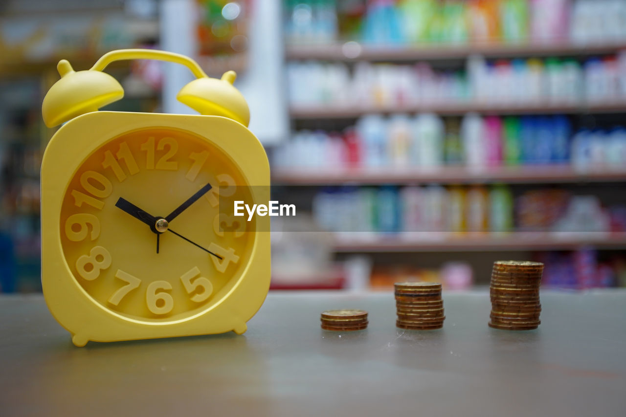 Close-up of yellow clock and coins on table 