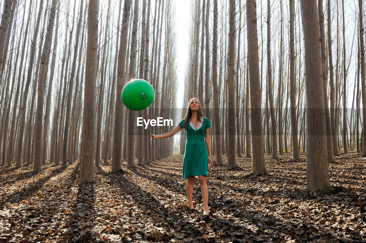 Full length of woman holding balloon while standing in forest