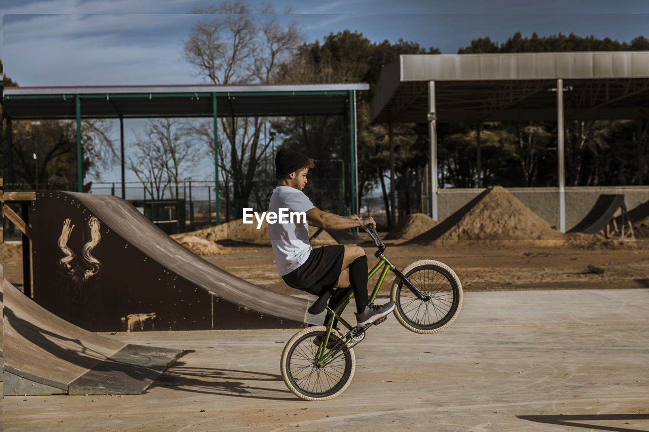Young man doing wheelie at bike park on sunny day