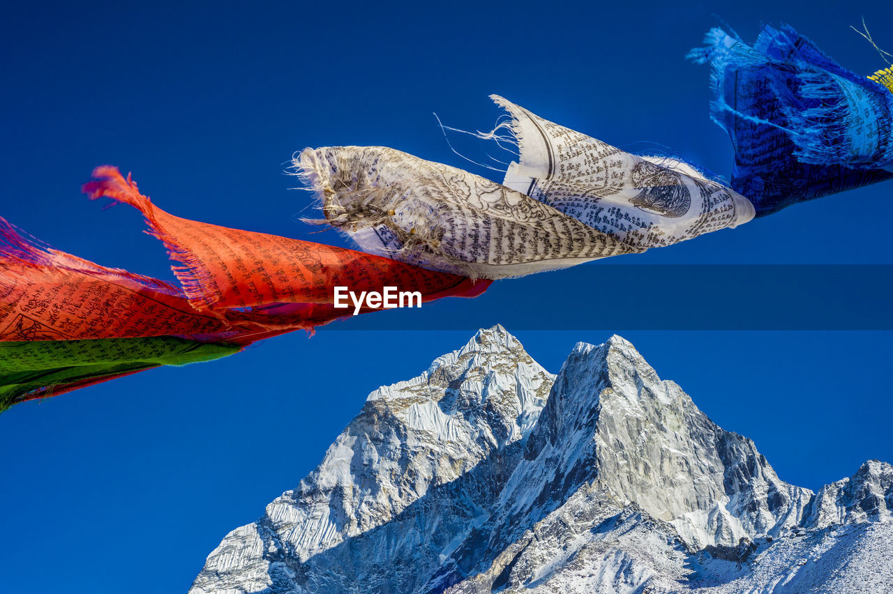 Low angle view of prayer flags and snowcapped mountain against clear blue sky