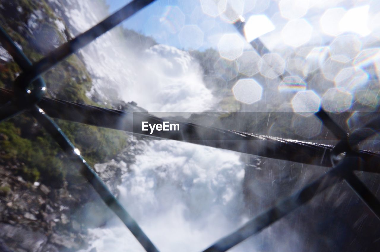 Low angle view of waterfall seen through metallic railing on sunny day