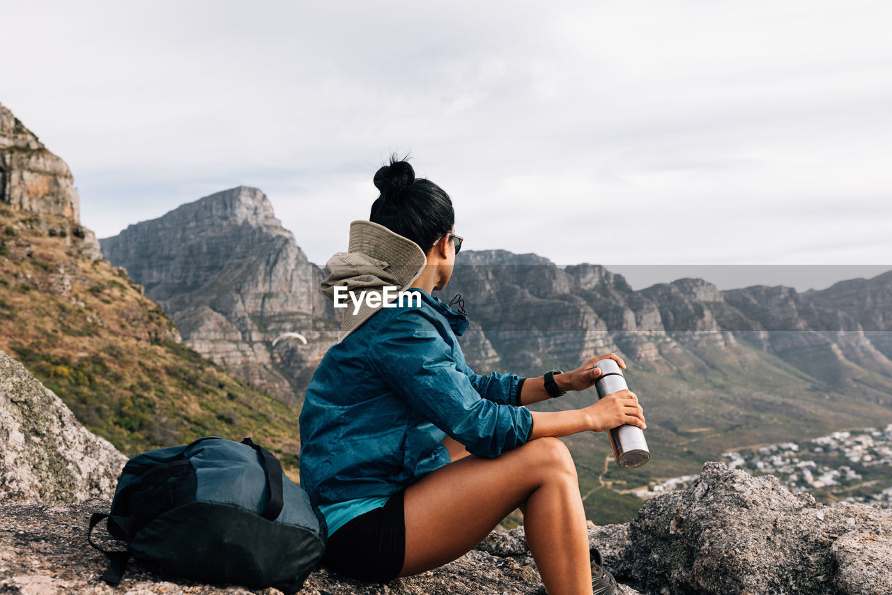 side view of man sitting on mountain against sky