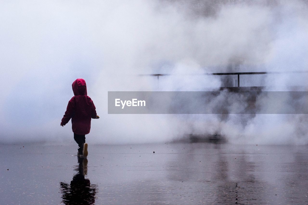 Rear view of girl walking on wet footpath against smoke