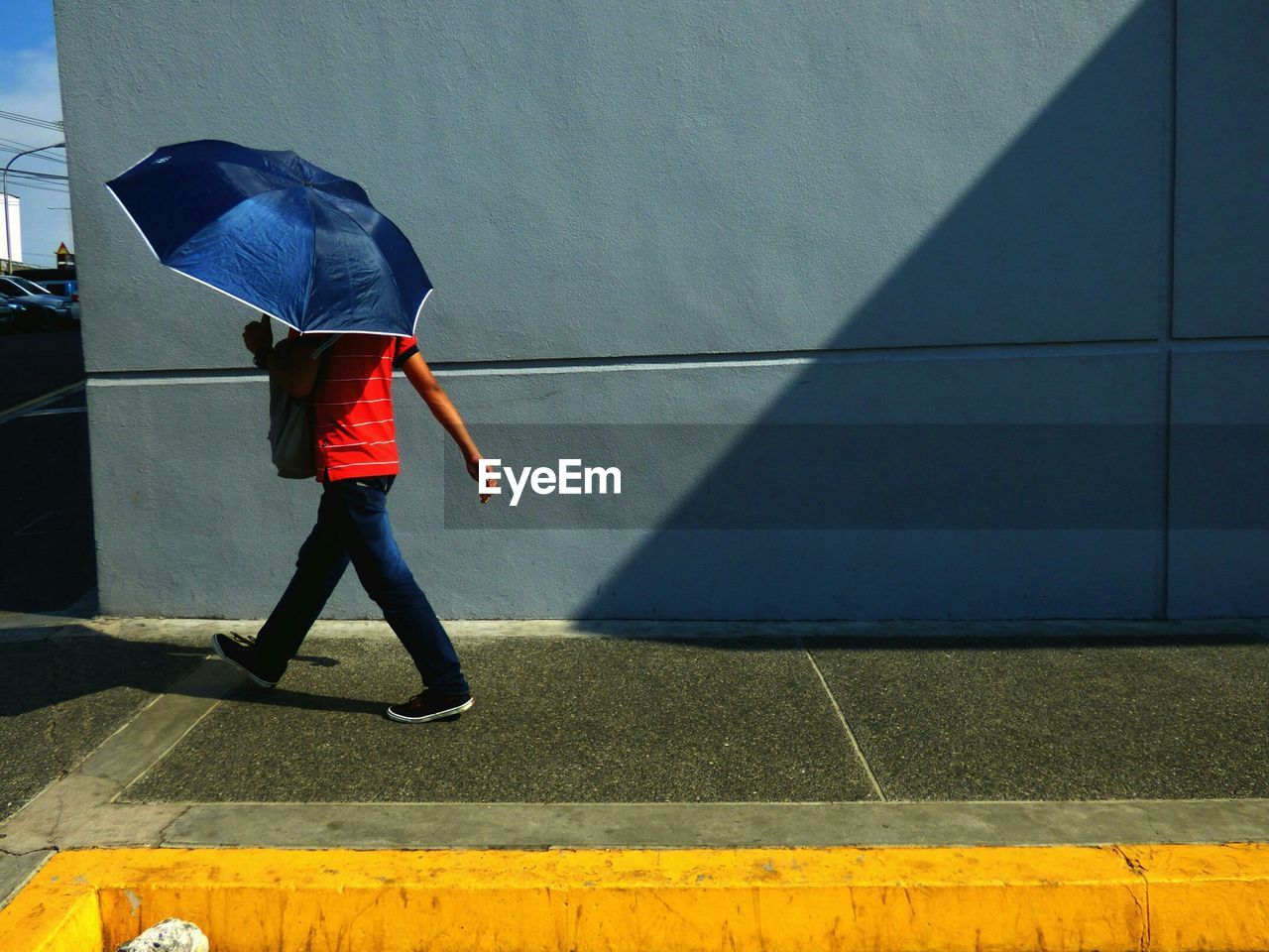 Man holding umbrella while walking against wall on sunny day