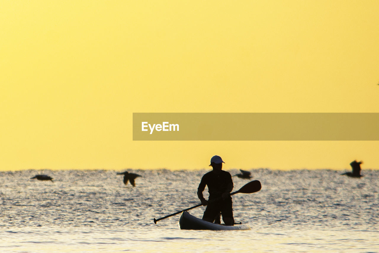 SILHOUETTE MAN ON SEA AGAINST ORANGE SKY