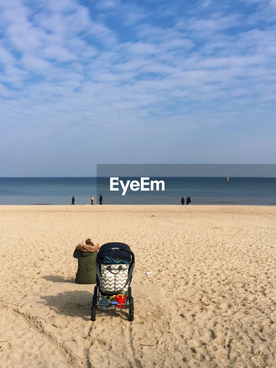 Rear view of woman with baby stroller sitting at beach against sky