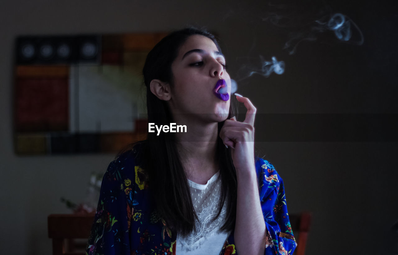 CLOSE-UP OF YOUNG WOMAN SMOKING AT HOME