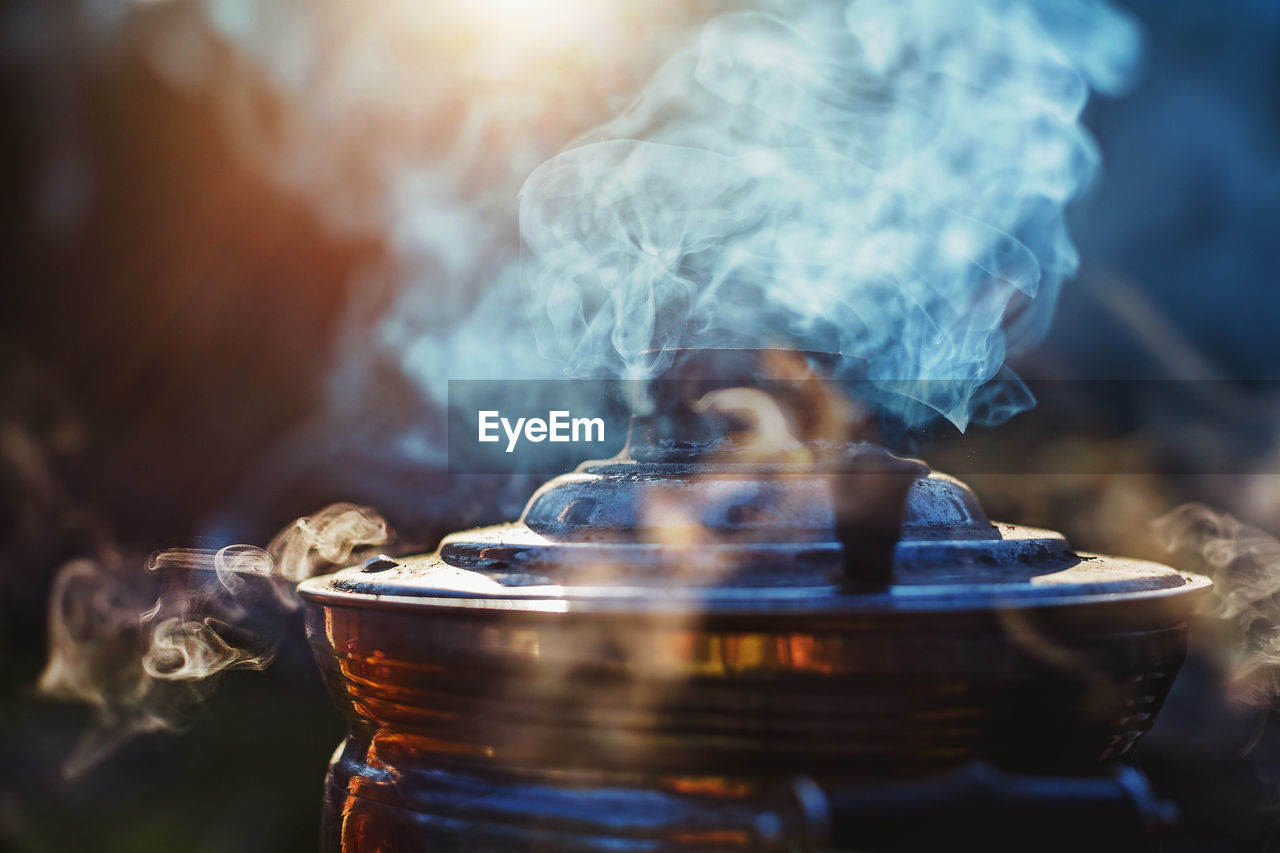Beautiful atmospheric smoke and mist rising from an old samovar with setting sun on background