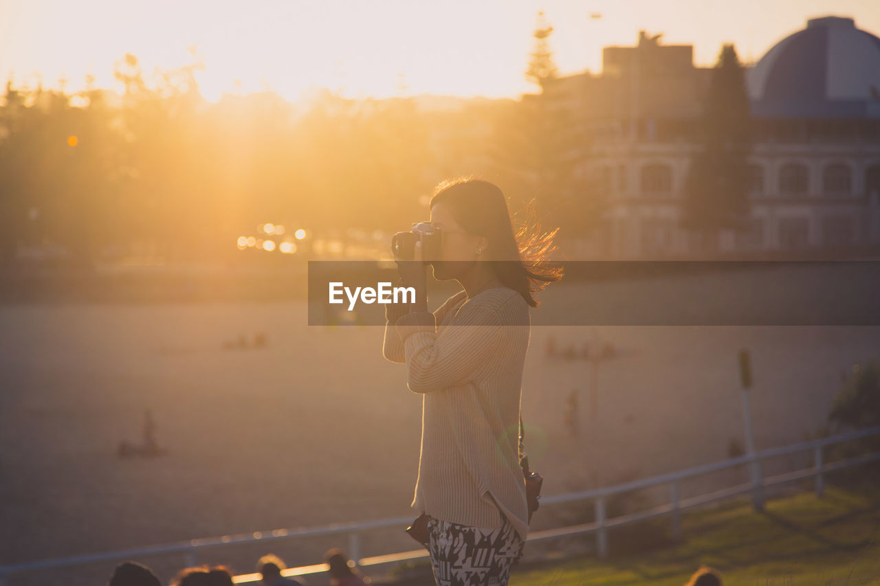 Woman photographing in park during sunset