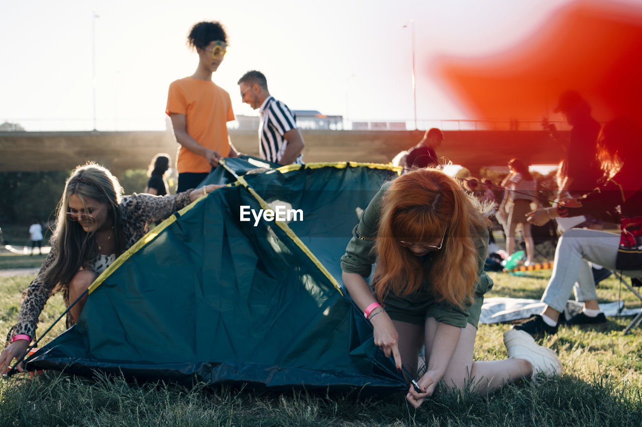Friends making tent on lawn in music festival during summer
