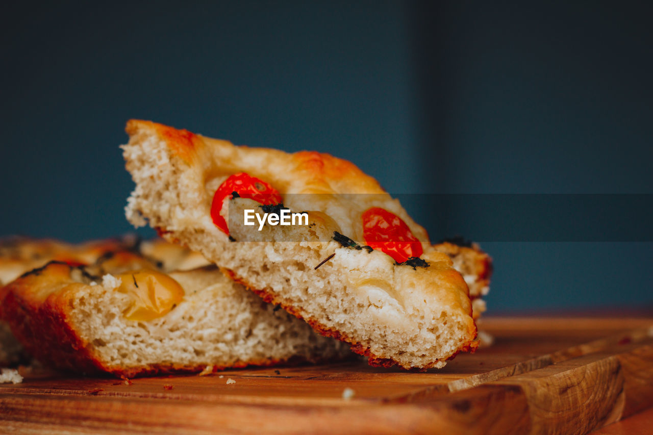 Homemade italian focaccia slices, with tomato and olive oil on a rustic wooden background.