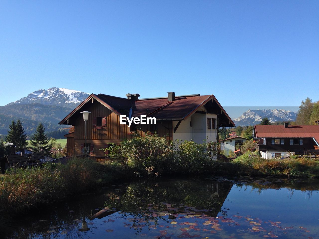 Houses by lake and buildings against clear blue sky