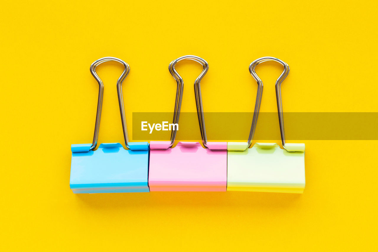 Close-up of multi colored binder clips against yellow background