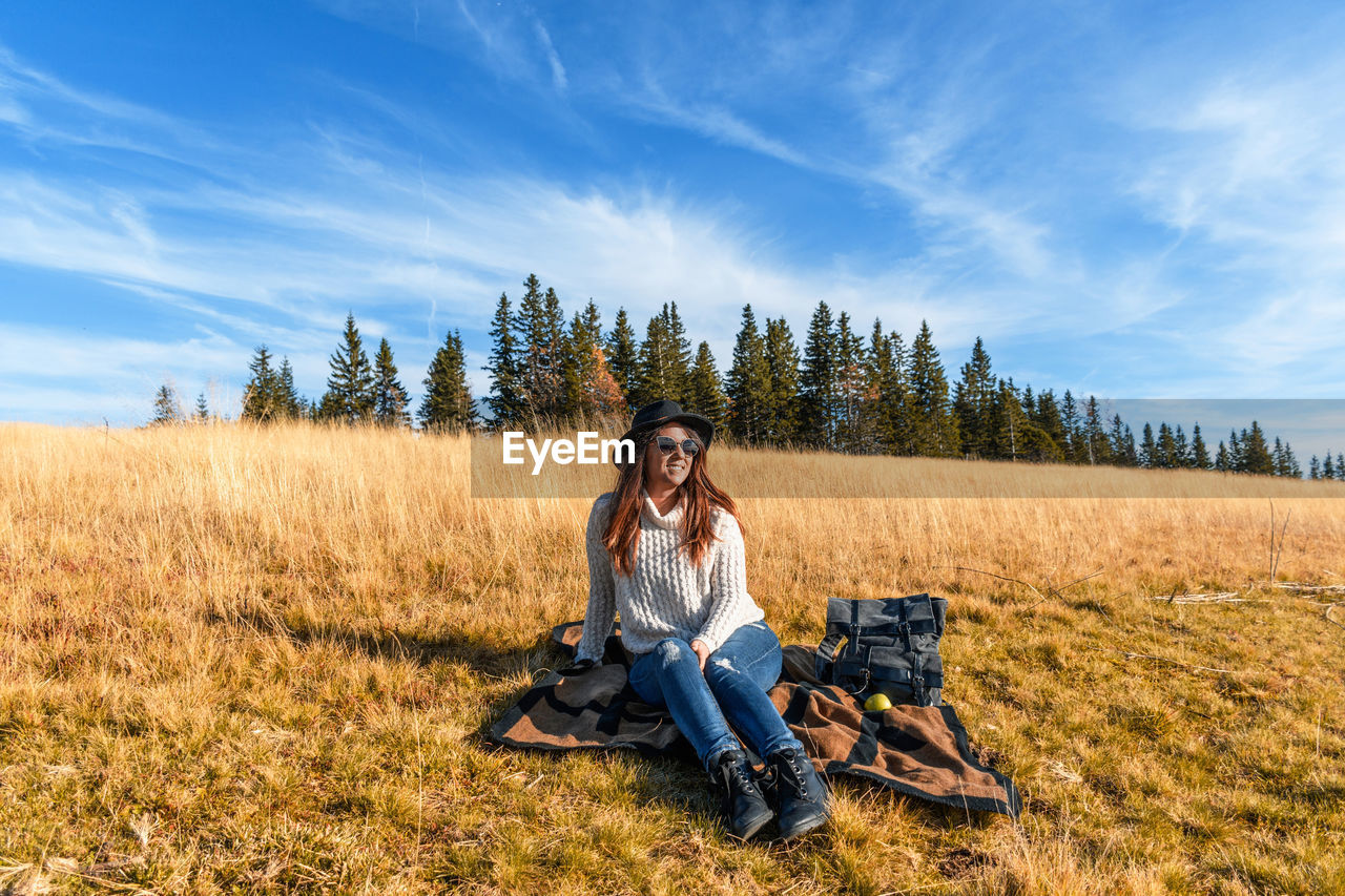 Woman sitting over picnic blanket on grass against sky