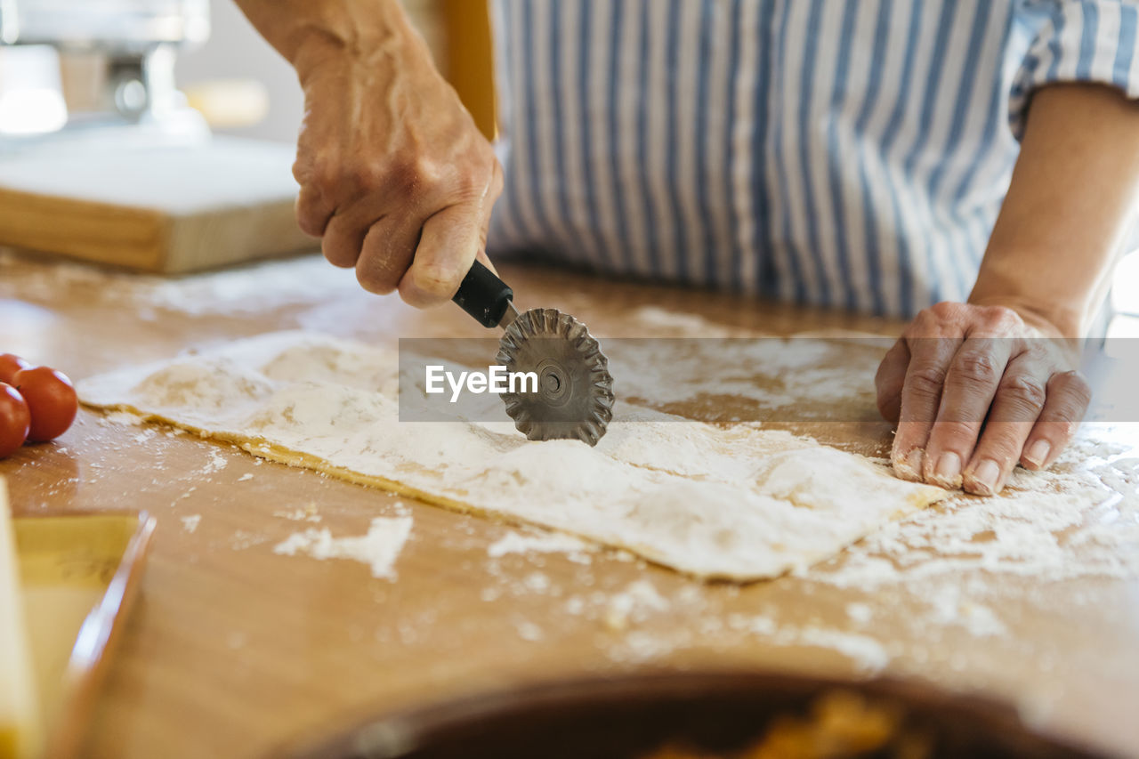 Woman cutting fresh ravioli, partial view