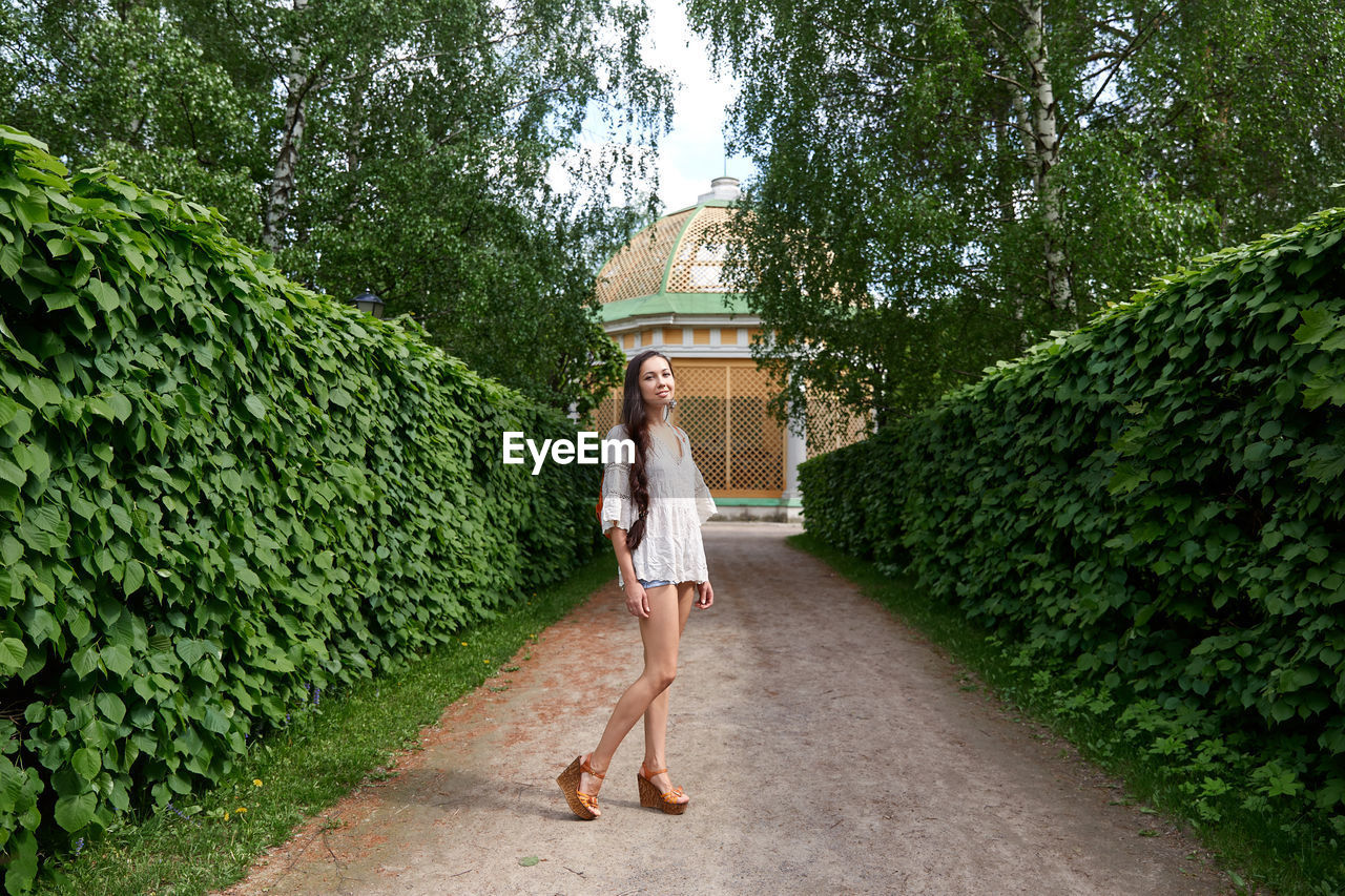 Full length portrait of woman standing on footpath amidst trees