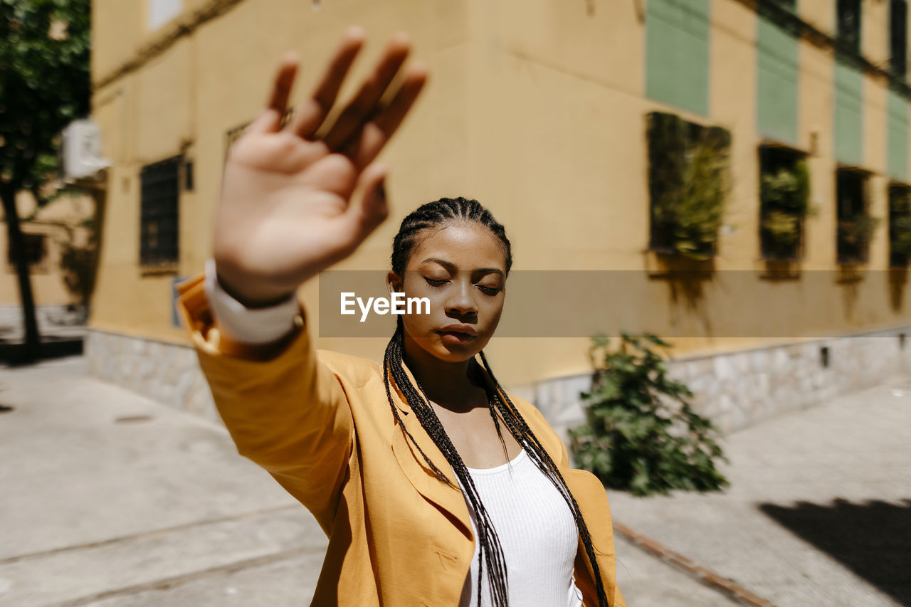 Young woman with hand raised standing in city during sunny day