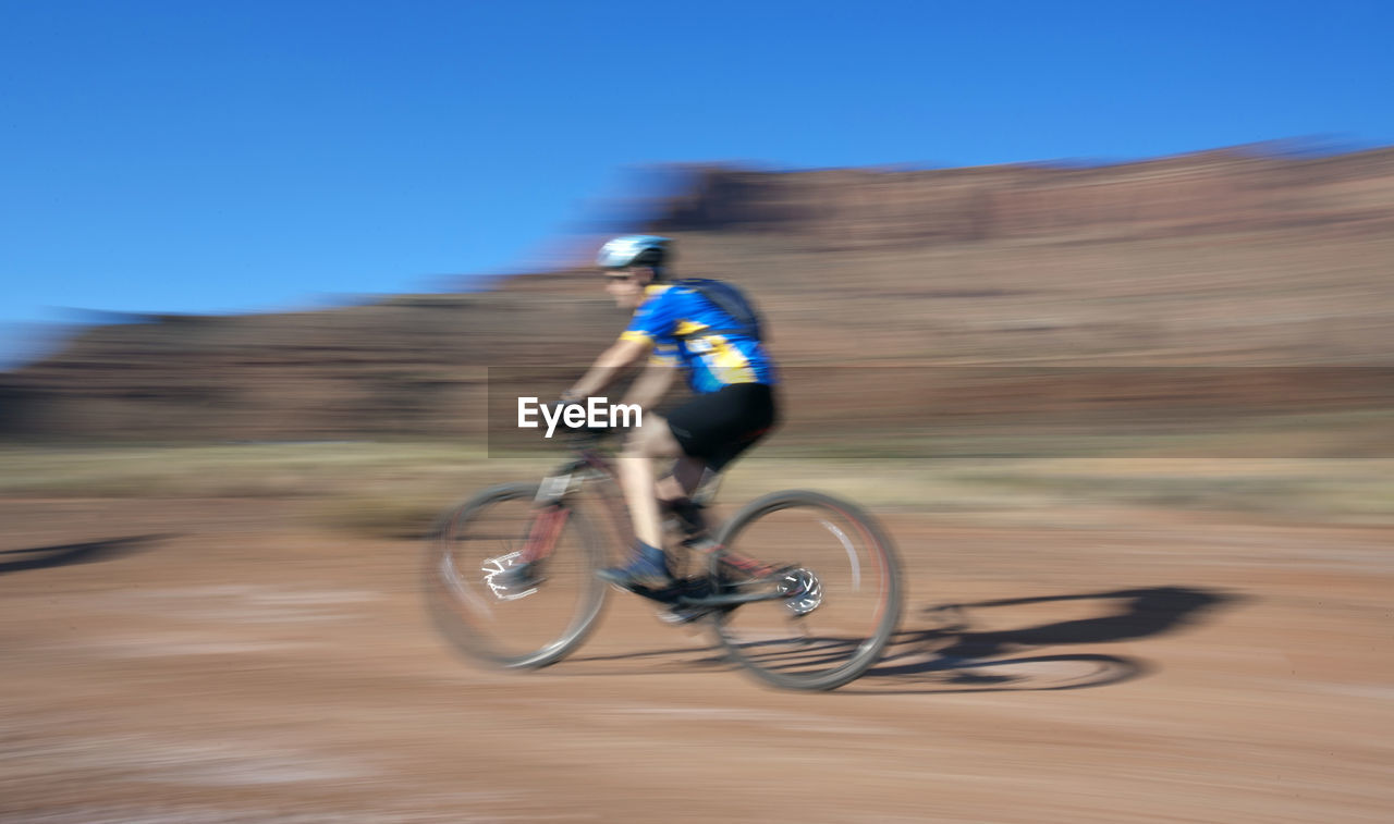 Blurred motion of man riding bicycle on landscape during sunny day