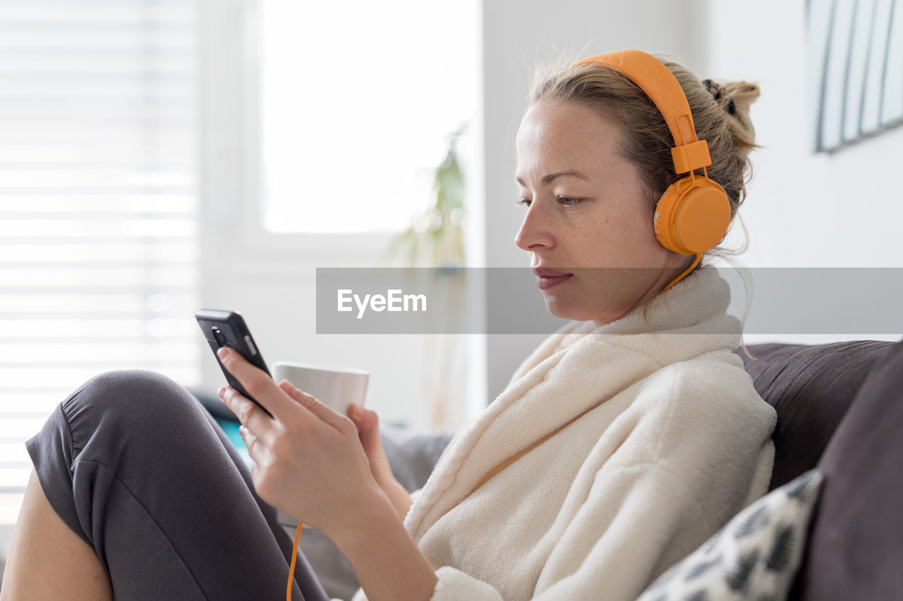 Mid adult woman listening music sitting on sofa at home