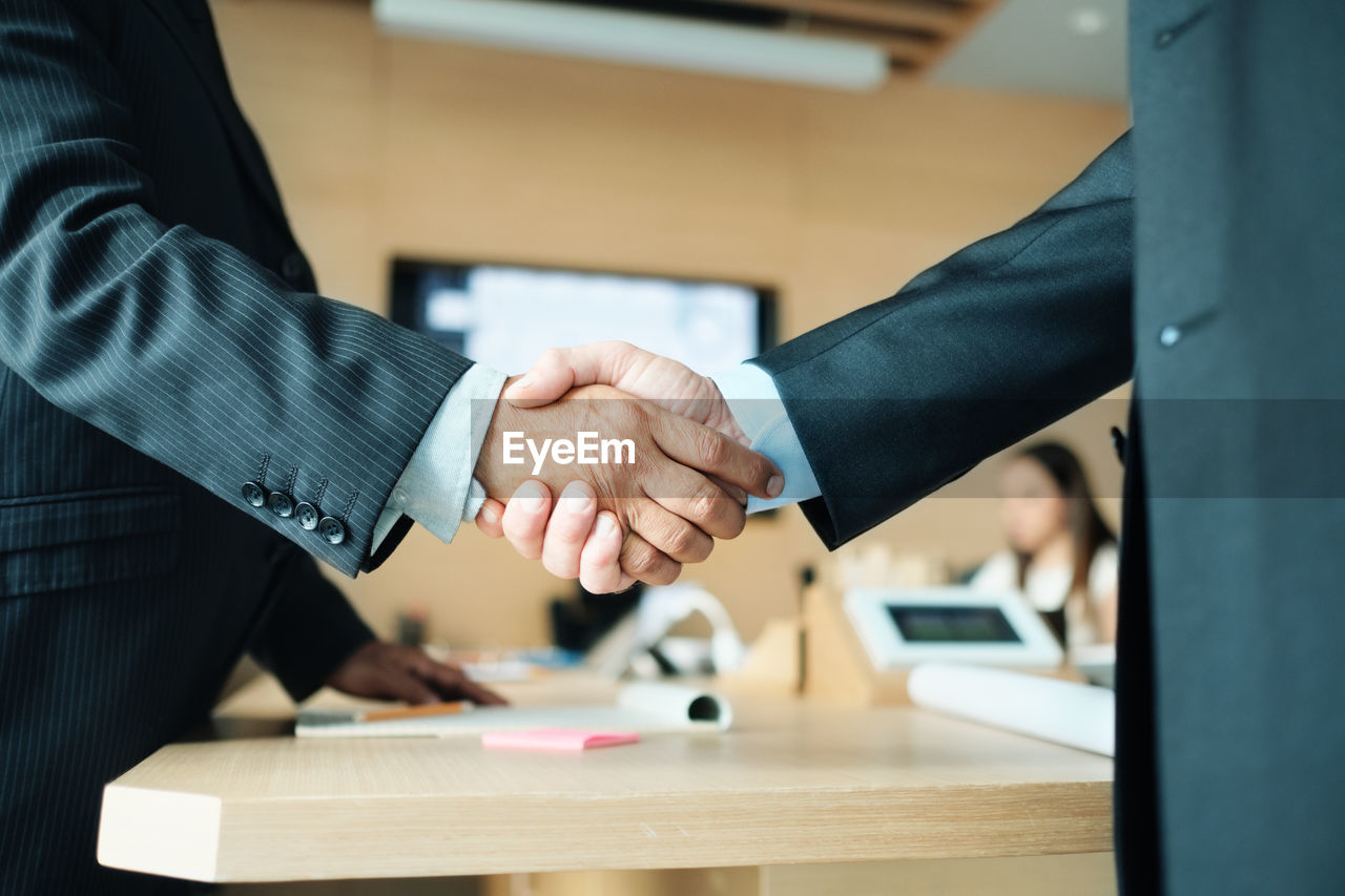 Midsection of male colleagues giving handshake in office