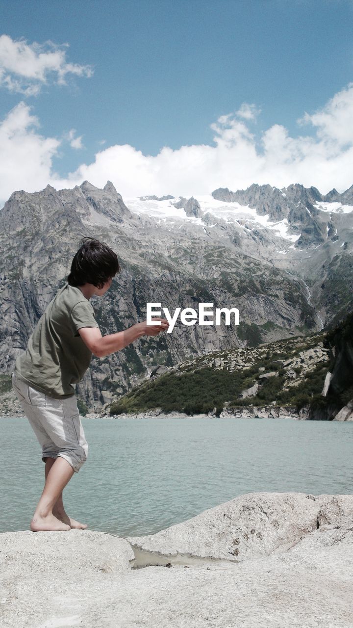 Boy standing on rock by lake against mountains