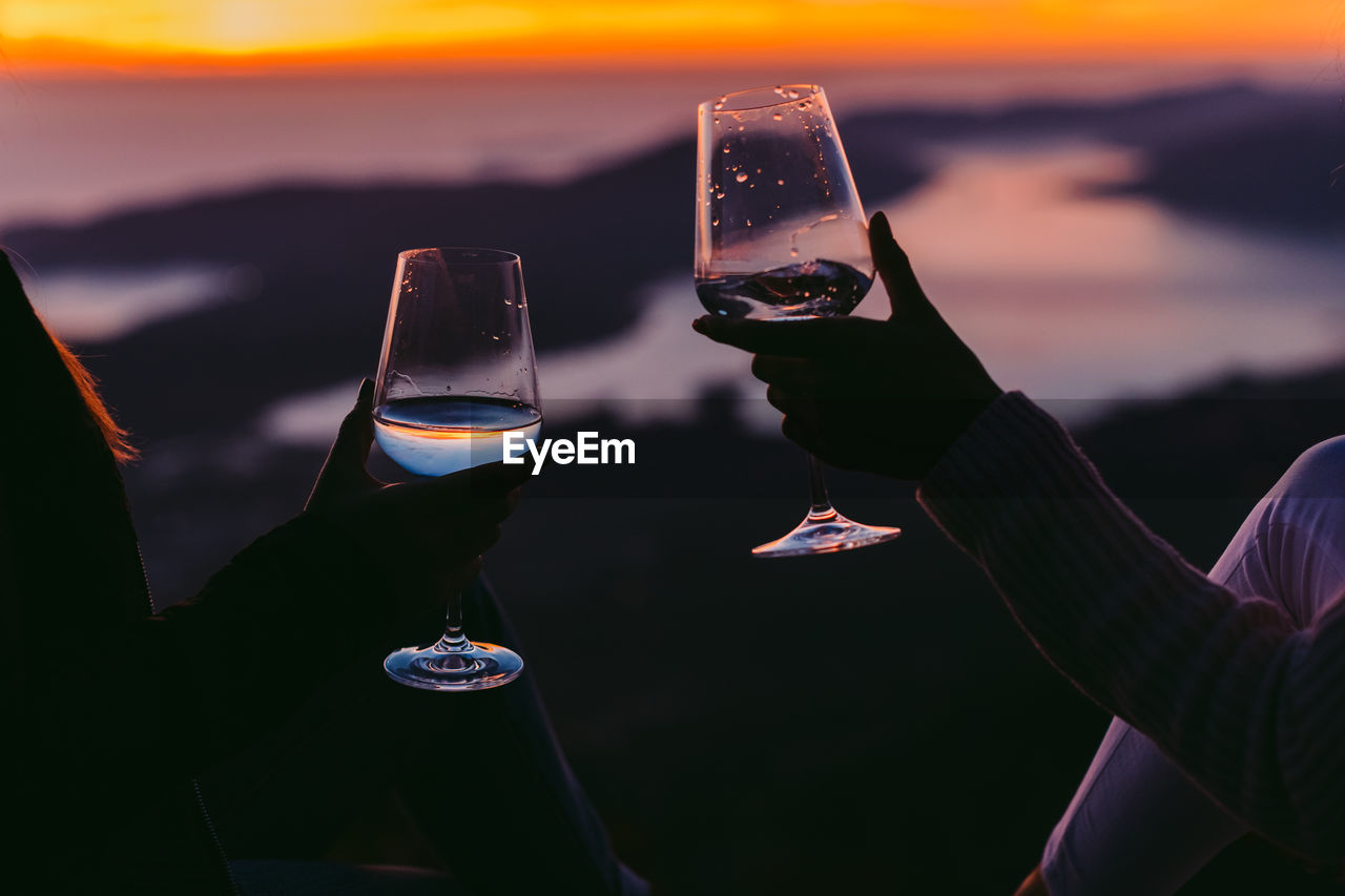 Cropped hands holding wine during sunset