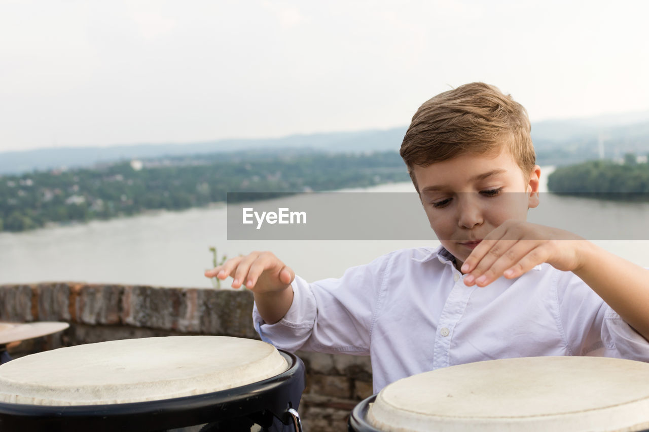 Boy playing bongo against river