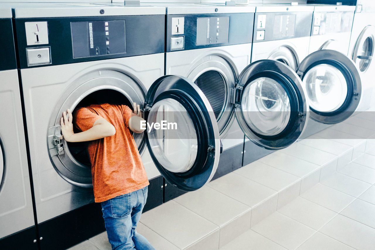 Boy looking in washing machine at laundromat