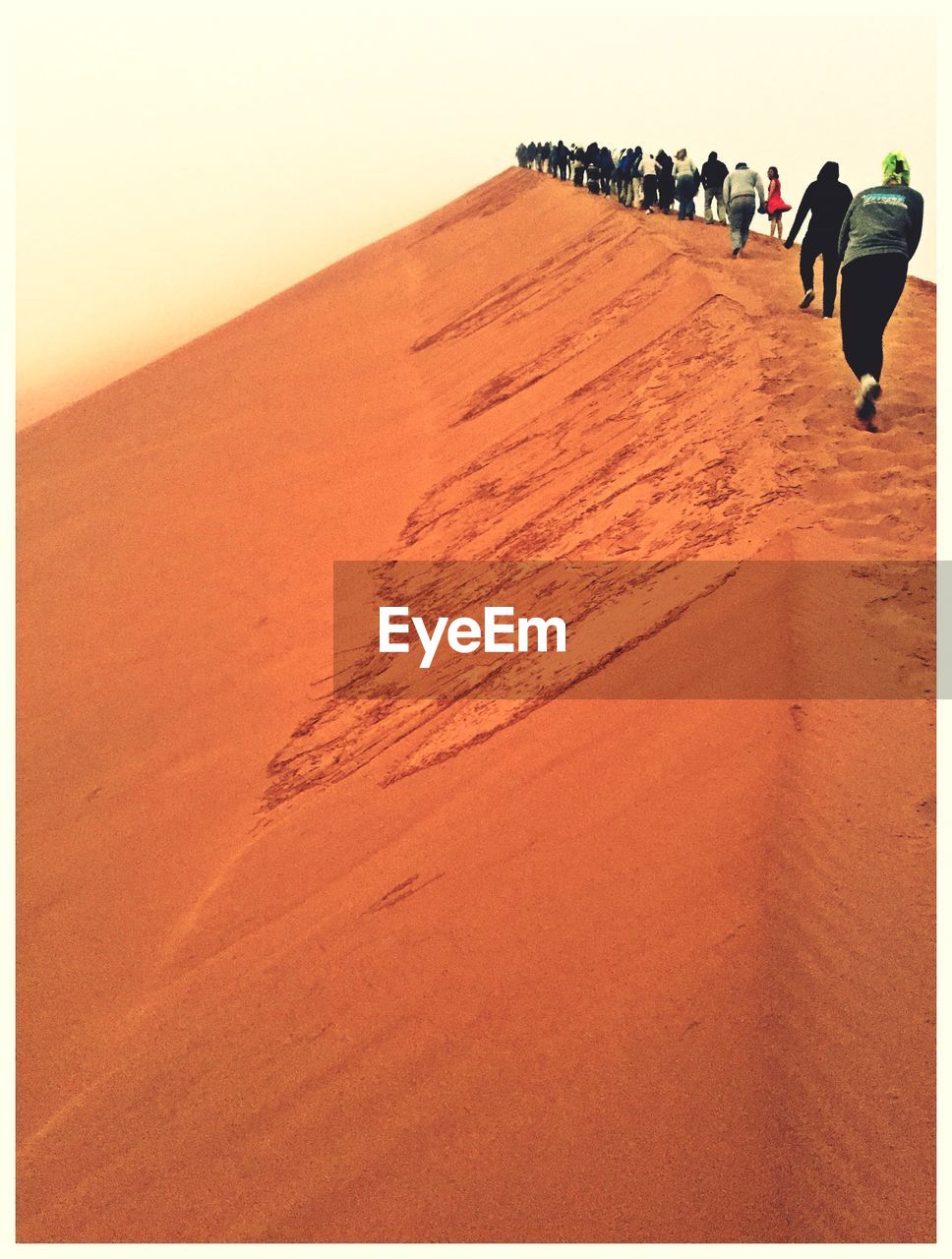 People walking in row over sand dune in desert against sky