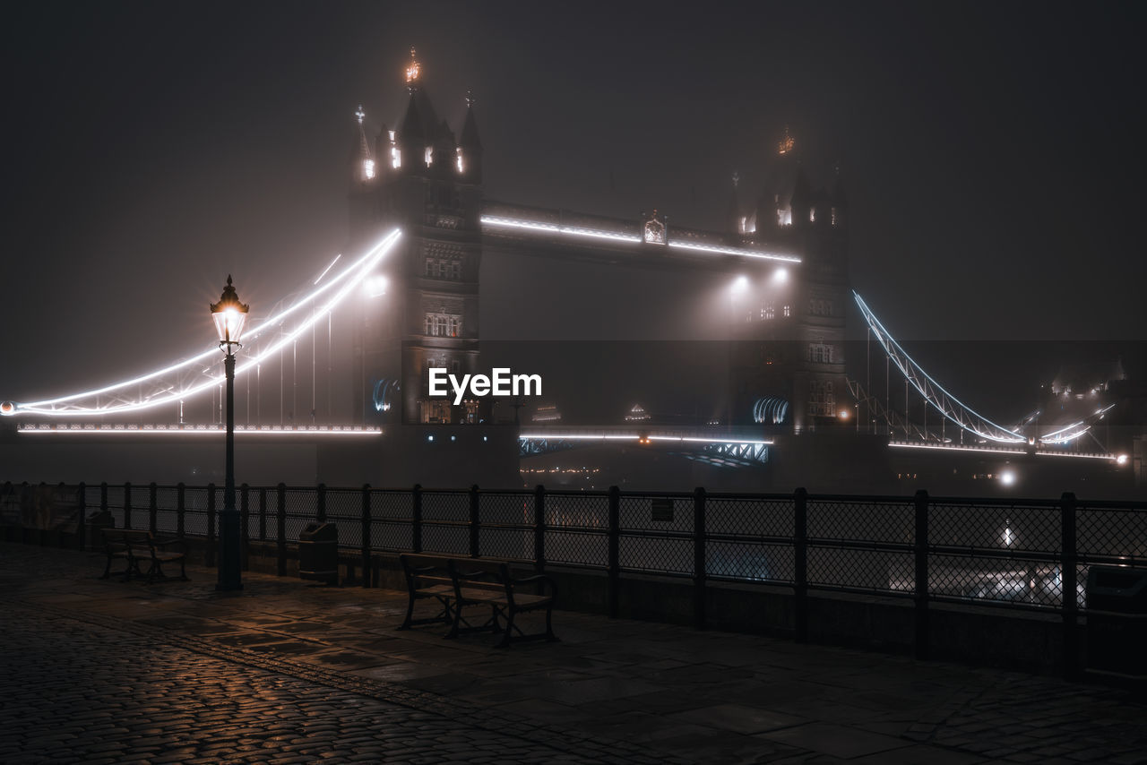 Illuminated bridge over river at night in fog