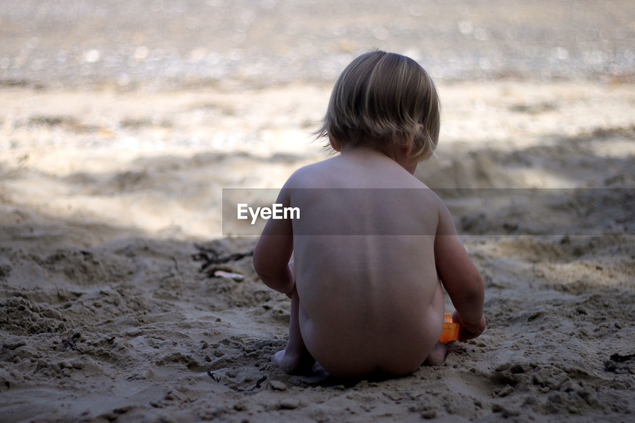 Rear view of naked baby boy playing on sand at beach