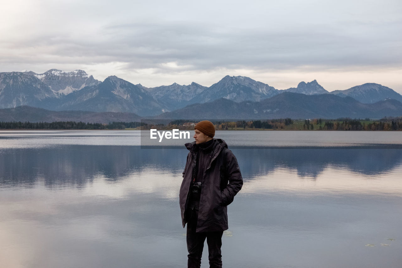 Man looking away while standing against lake