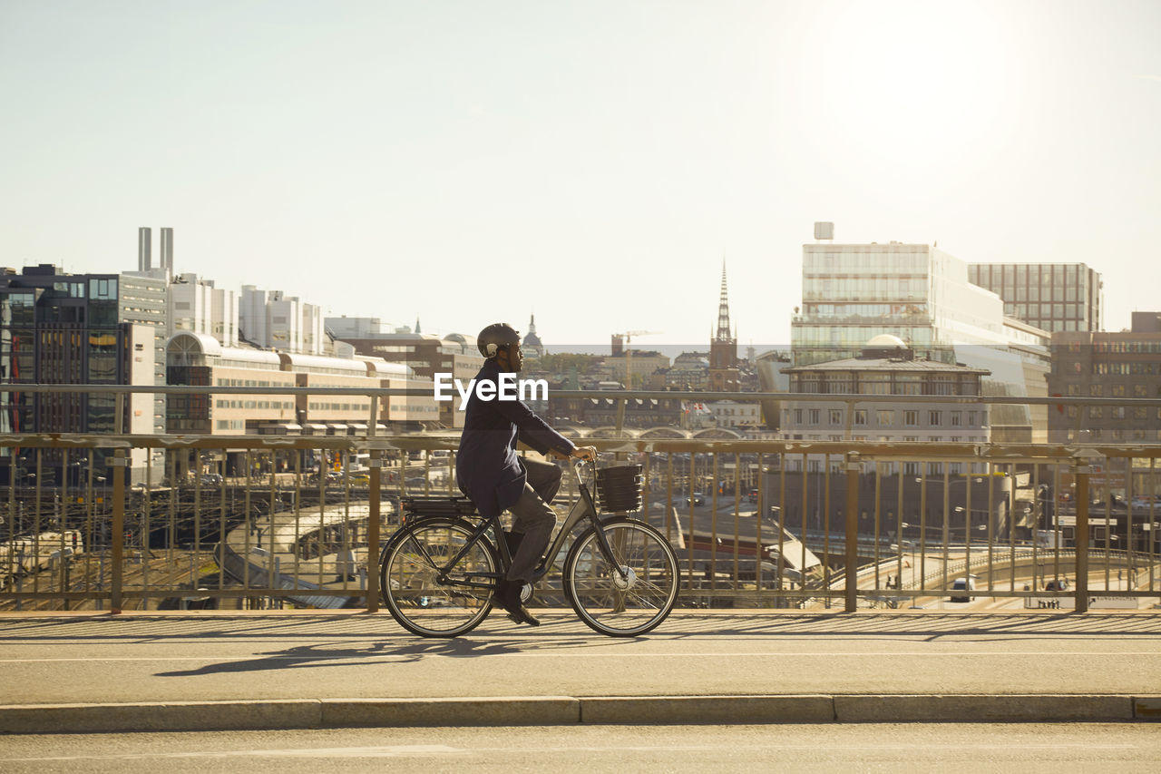 Full length side view of young man riding electric bicycle on bridge in city