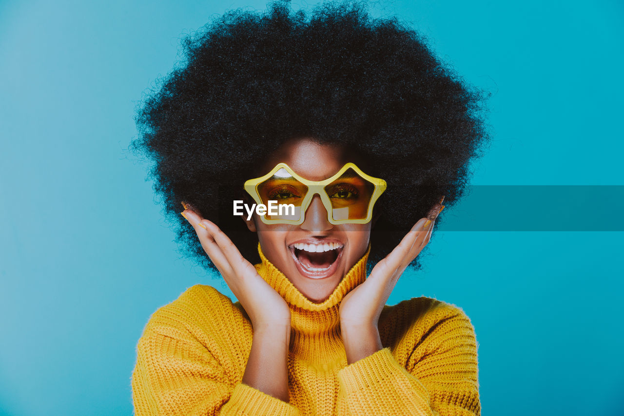 Portrait of happy young woman wearing sunglasses against blue background