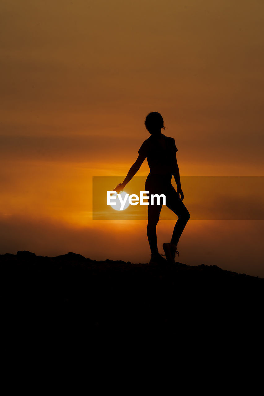 side view of silhouette man standing on field against orange sky