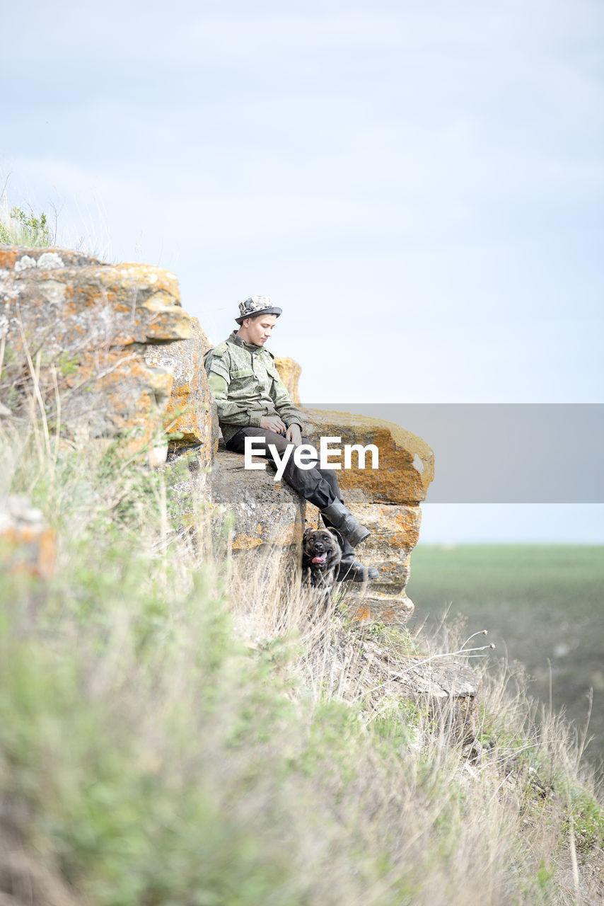 Man sitting on mountain against sky