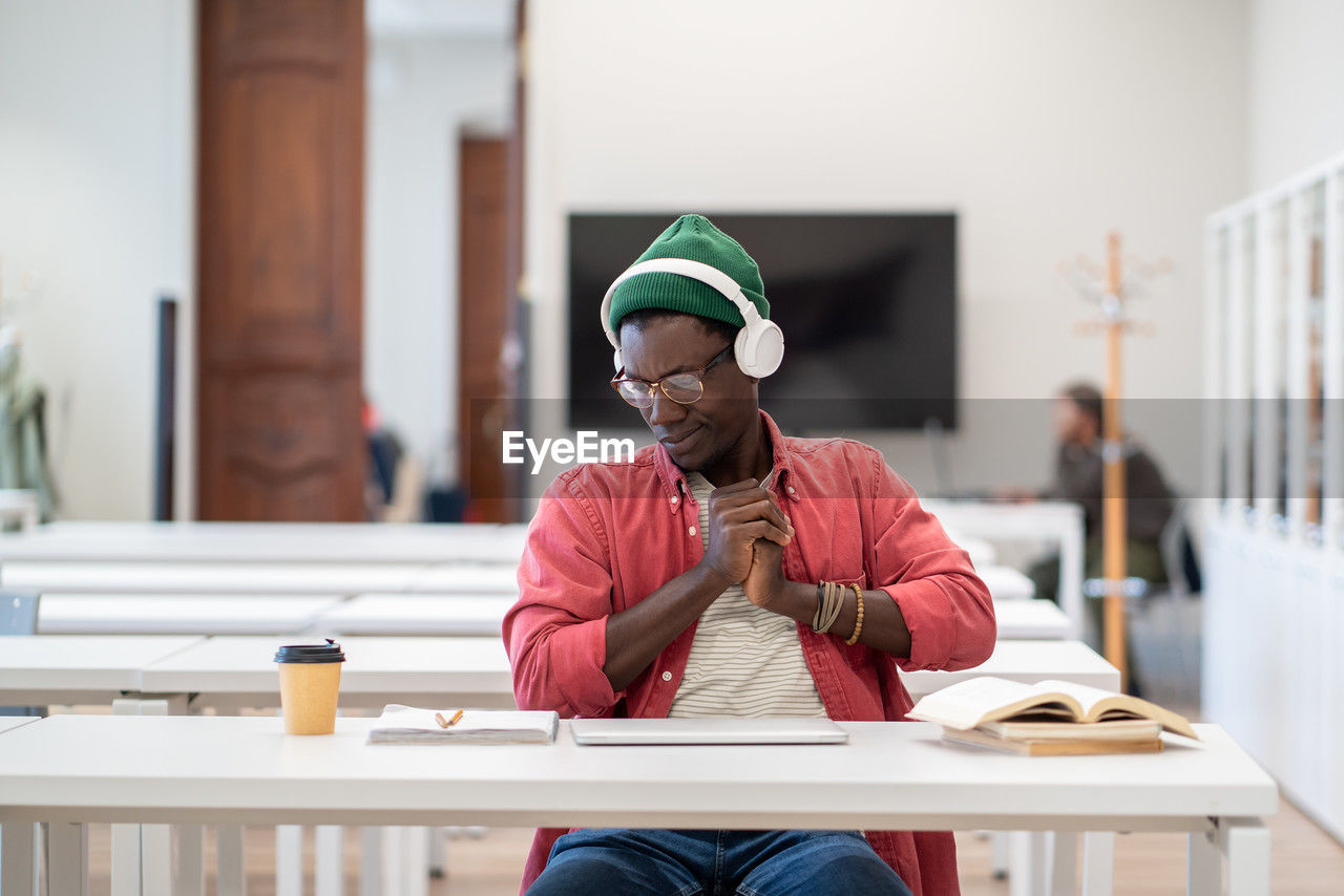 Tired sleepy black guy student in headset stretch on chair exhausted after long time study at laptop