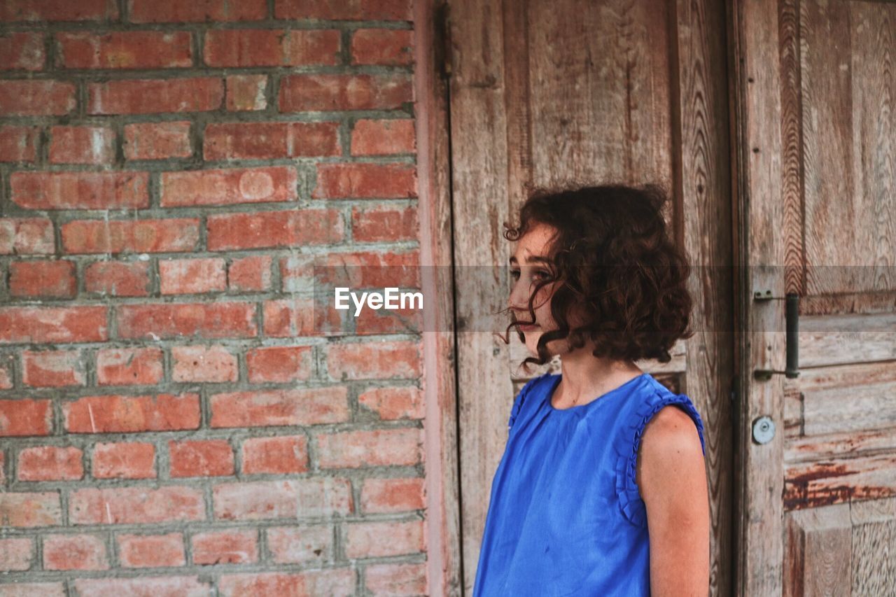 Girl looking away while standing by brick wall