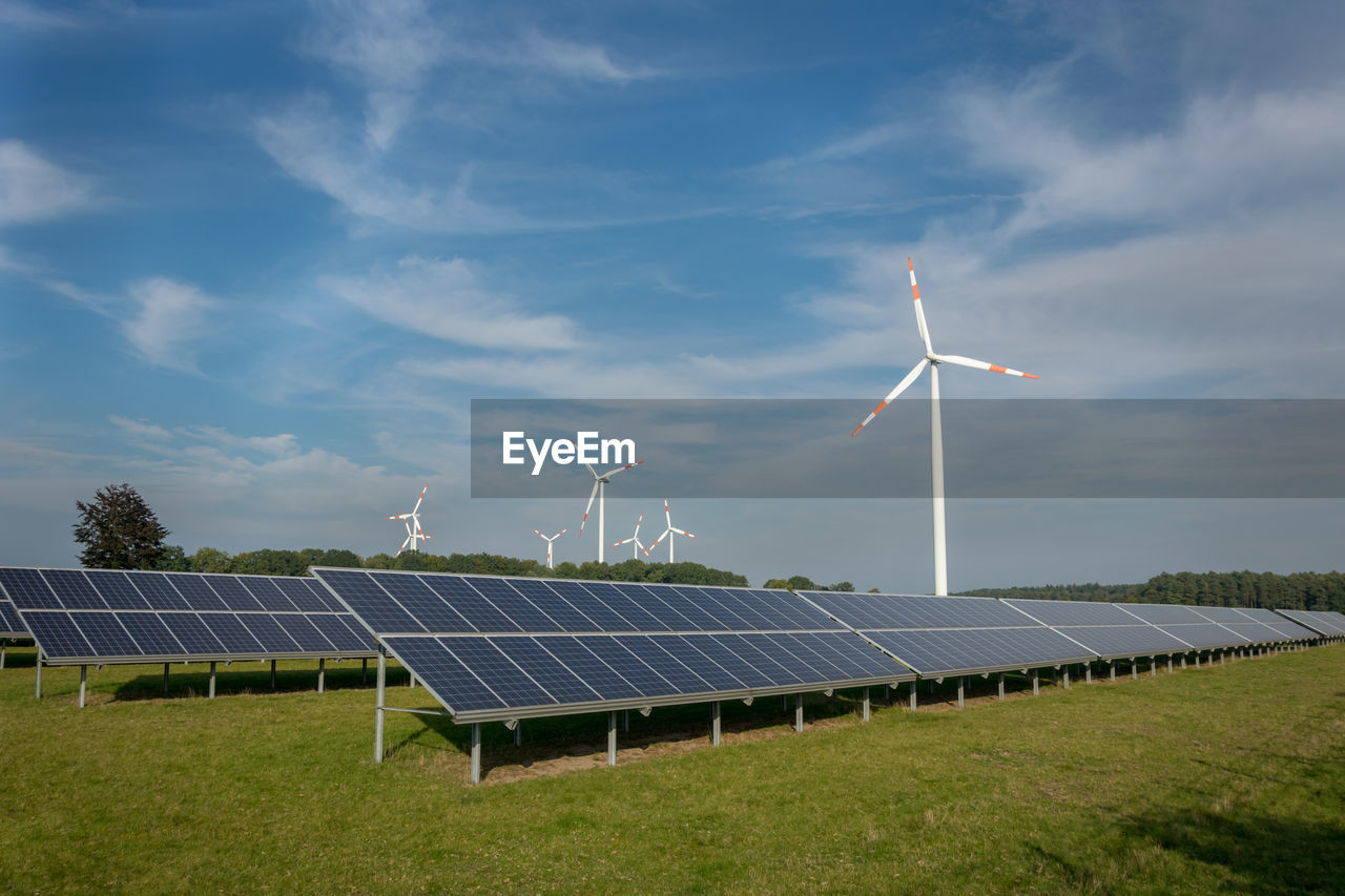 Wind turbines and solar panels on field against sky