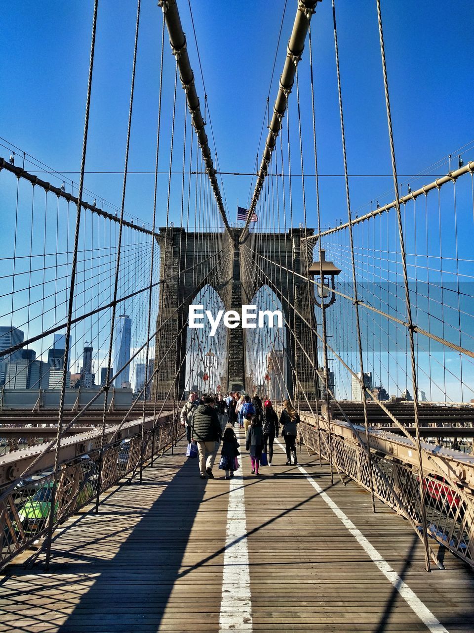 People walking on brooklyn bridge against blue sky