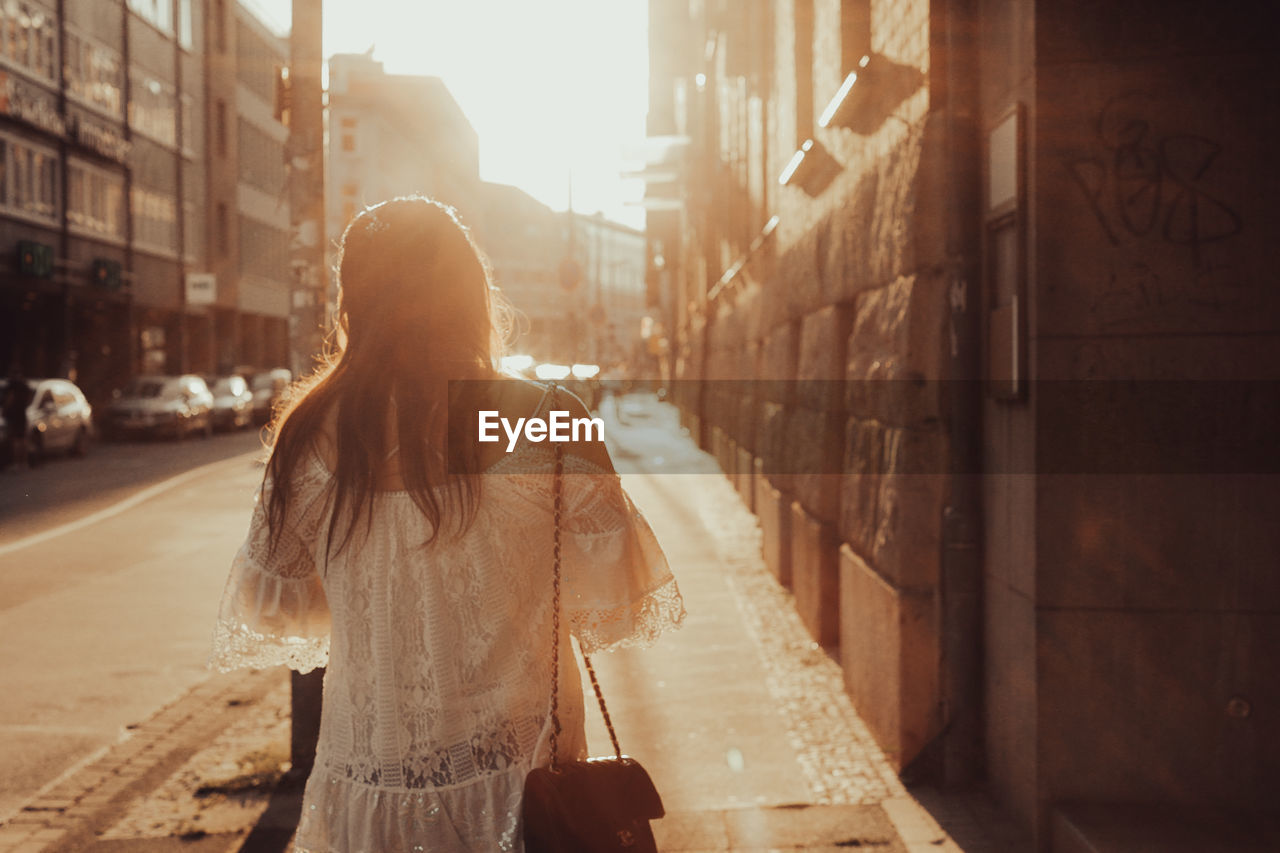 Rear view of woman walking on street in city at sunset