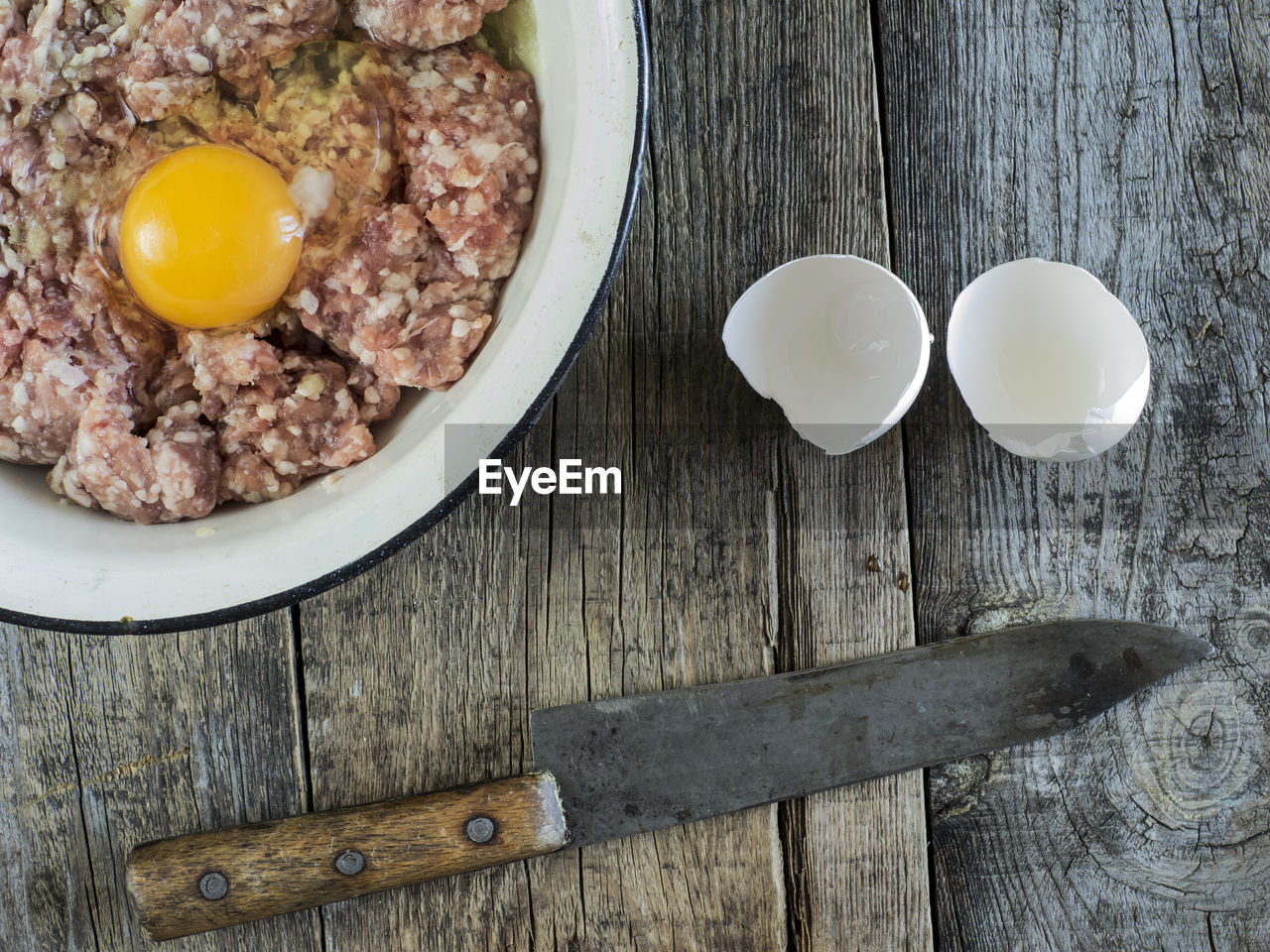 Directly above shot of minced meat with egg yolk in bowl by knife on table