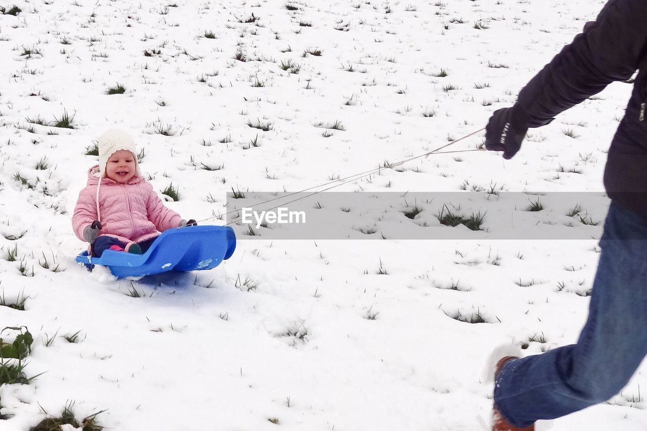 Low section of man pulling sled with child on snow covered field