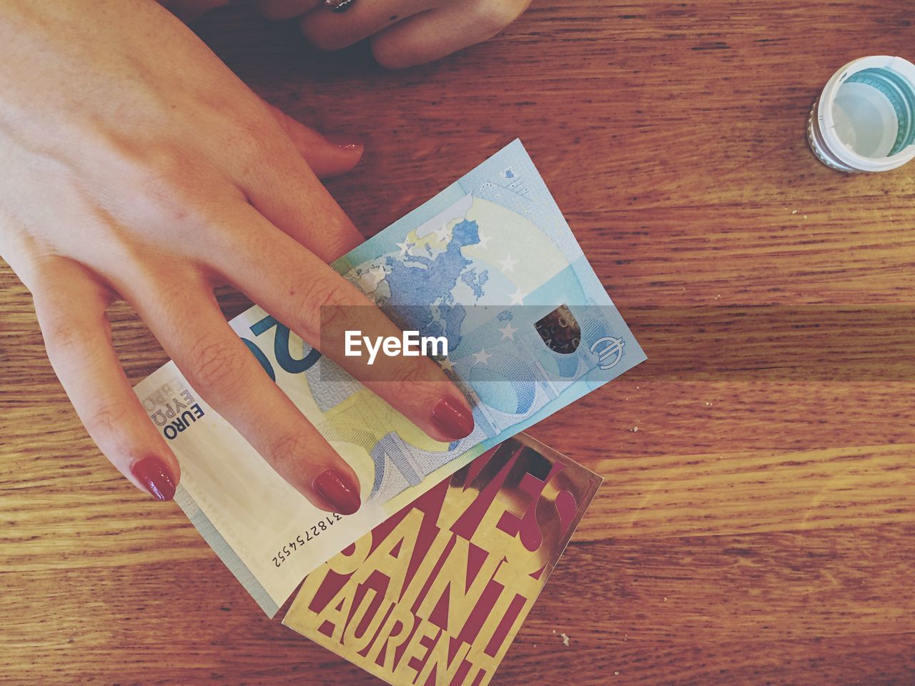 Cropped image of hand holding twenty euro banknote over wooden table