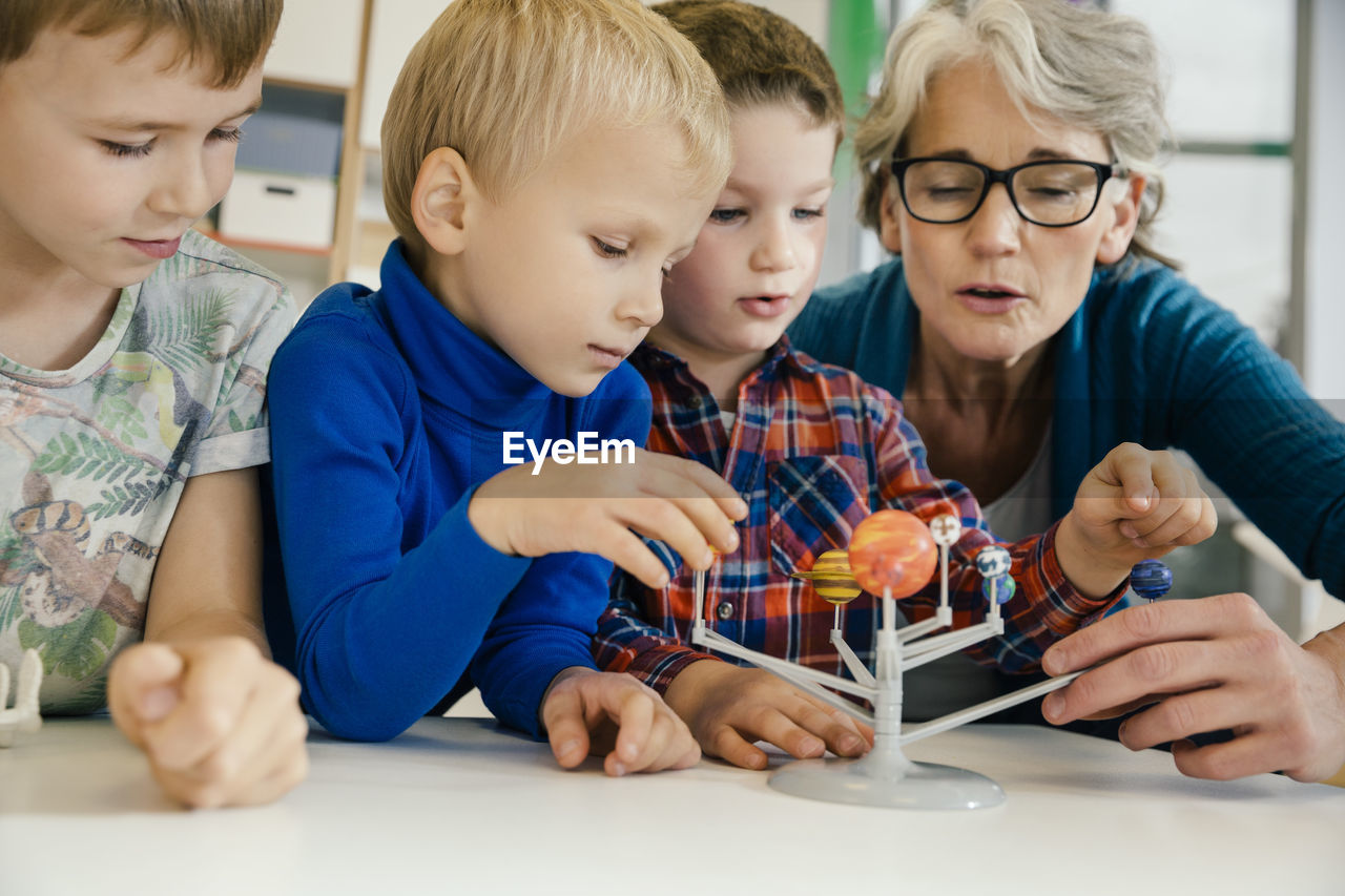 Pre-school teacher explaining solar system model to boys in kindergarten