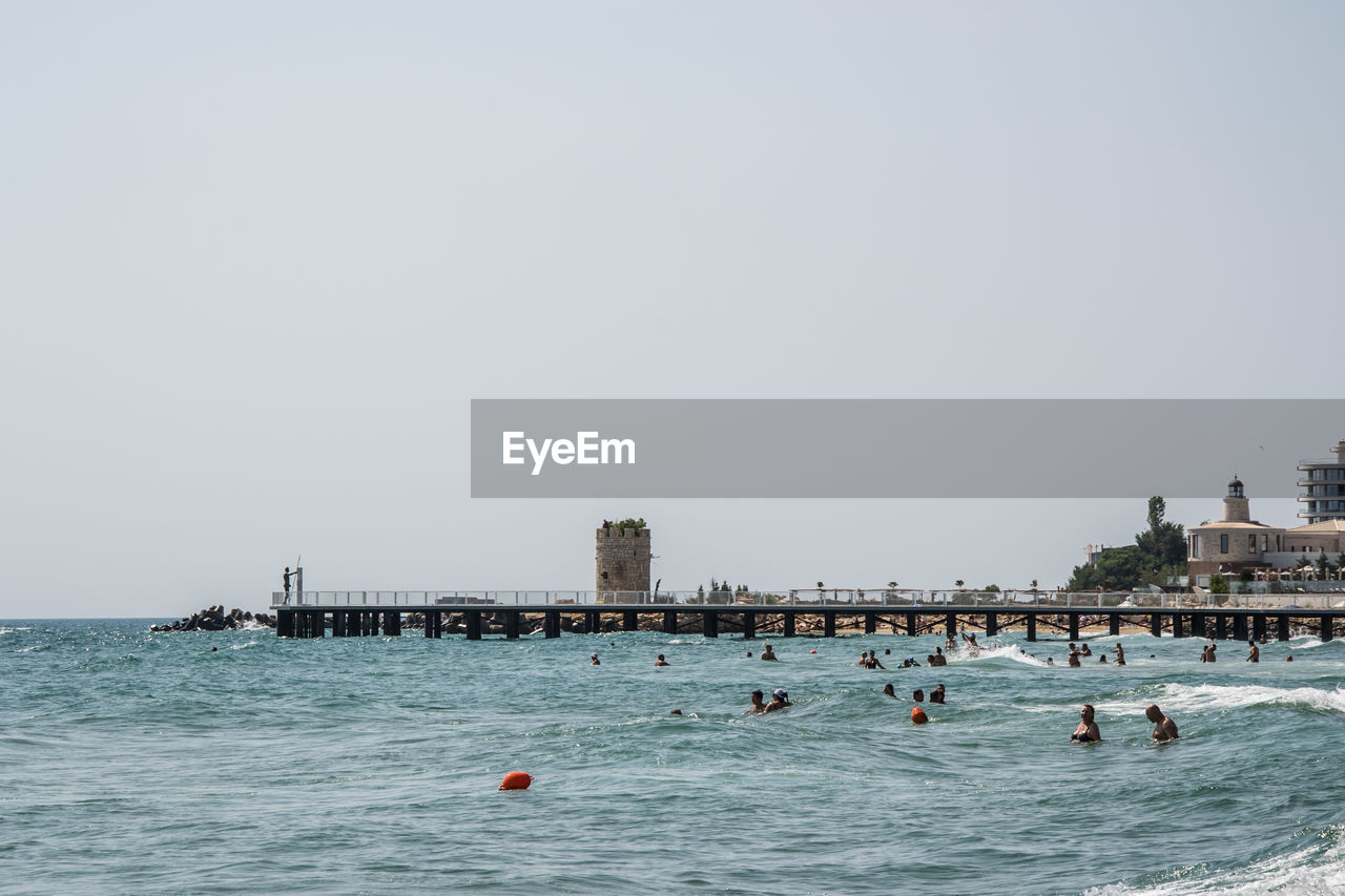 GROUP OF PEOPLE IN SEA AGAINST CLEAR SKY